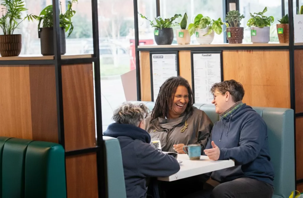 Three older women sitting in a cafe laughing and having coffee