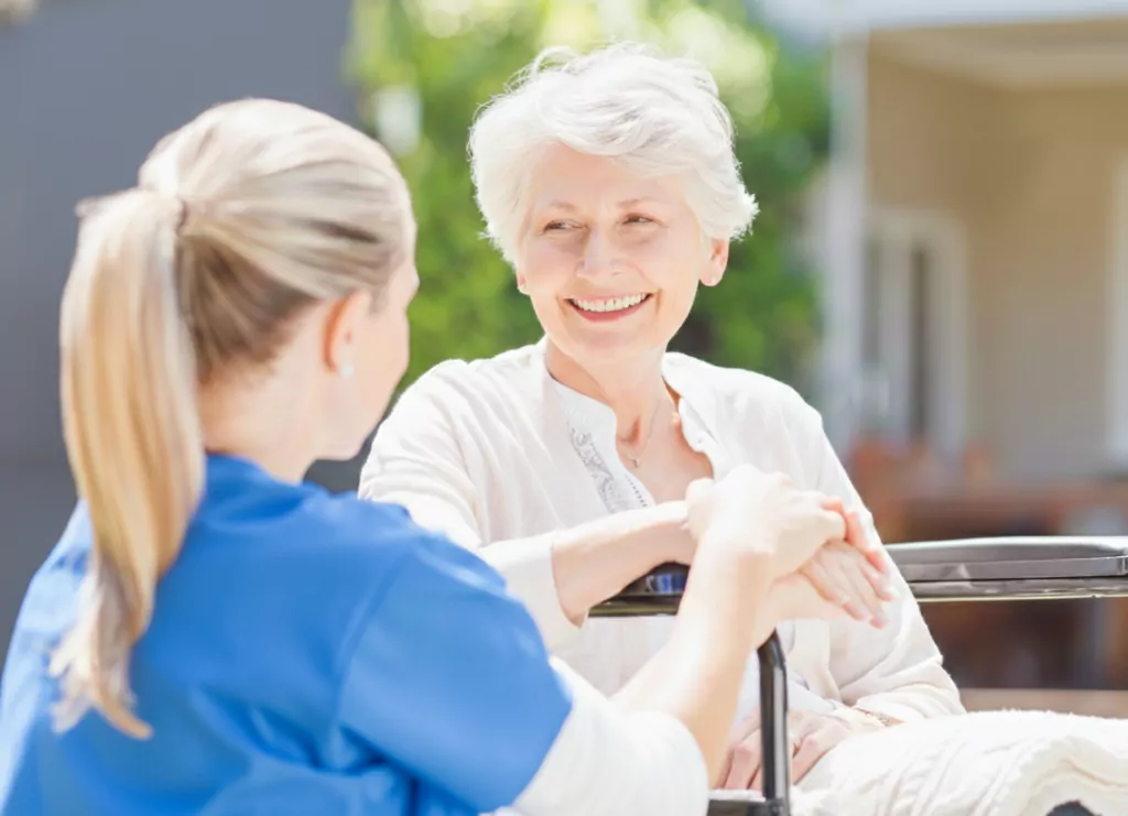 A Community Care TASMANIA female carer sitting next to an older woman in her wheelchair, holding her hand.